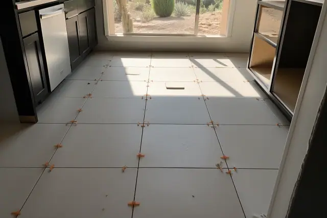 Ceramic tile floor installation with spacers and dust in a kitchen in Phoenix, AZ, with desert views through a window.