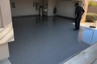 Contractor inspecting a finished epoxy garage floor with sunlight and stucco walls in Phoenix, AZ.