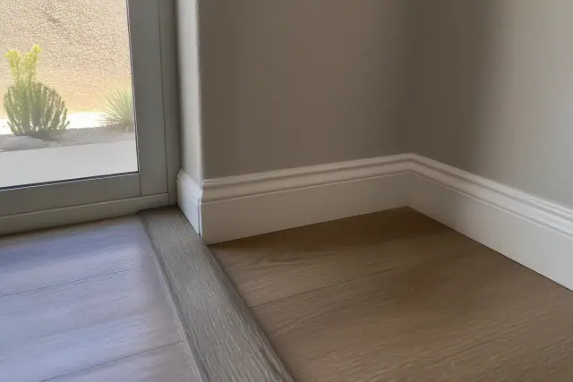 A close-up of a transition strip and baseboard corner installed on a laminate floor at a jobsite in Phoenix, AZ.