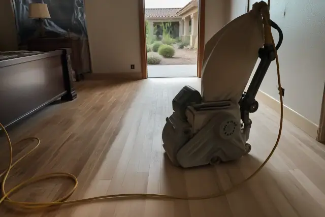 Industrial sander smoothing hardwood floor planks in a bedroom during a renovation in Gilbert, AZ.