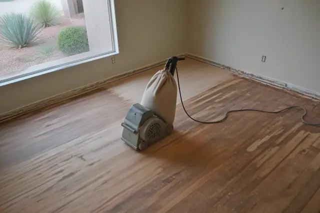 Industrial sander smoothing hardwood floor planks during a home restoration project in Tempe, AZ.