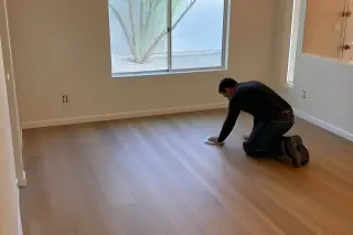 Contractor wiping dust from new oak-look luxury vinyl planks in a Phoenix, AZ home living room.