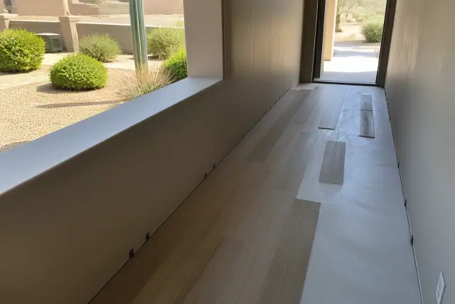 Worker installing luxury vinyl planks in a narrow hallway with a view of a xeriscaped front yard in Mesa, AZ.