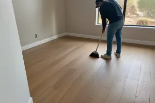 Technician sweeping dust after a finished flooring installation in a Phoenix, AZ office with desert views.