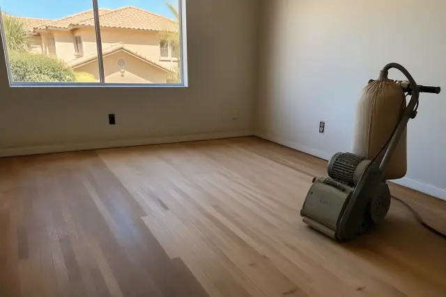 Industrial sander smoothing raw hardwood floor planks in a bedroom under renovation in Goodyear, AZ.