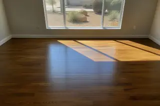 Smooth, glossy stained hardwood flooring in a sunlit bedroom with a view of a xeriscaped yard in Phoenix, AZ.