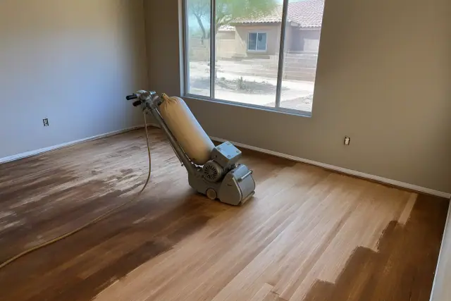Industrial sander stripping old finish from hardwood flooring during a renovation in Chandler, AZ.