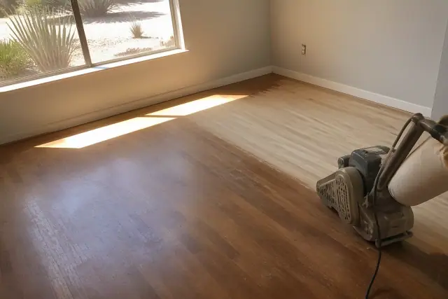 Industrial sander smoothing hardwood planks during a floor restoration in a Phoenix, AZ home.