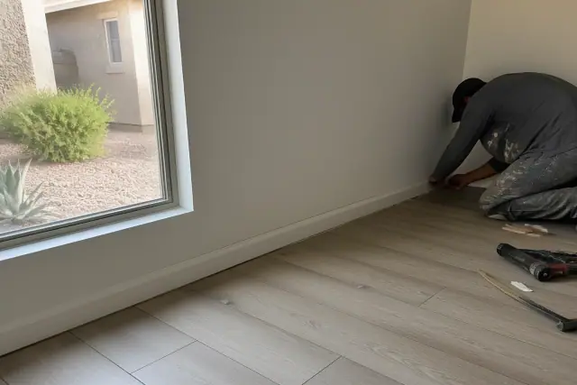 Contractor trimming baseboards along newly installed laminate flooring in a Peoria, AZ home.