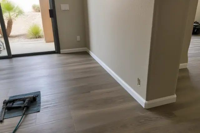 New laminate flooring installation with baseboards being secured in a residential living space in Goodyear, AZ.