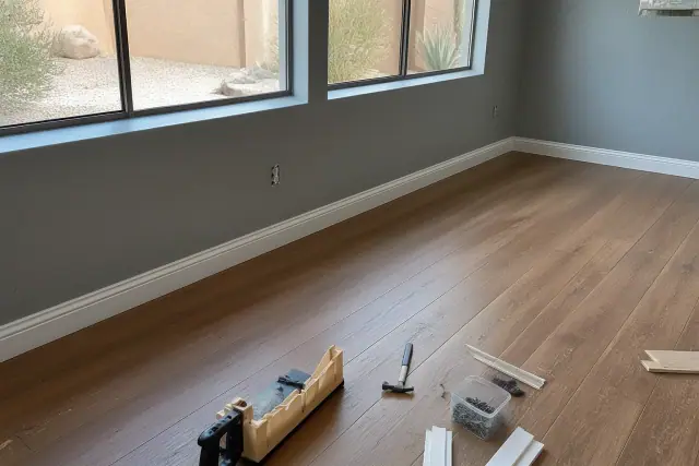Laminate flooring installation meeting baseboards with tools on the floor of a basement in Mesa, AZ.