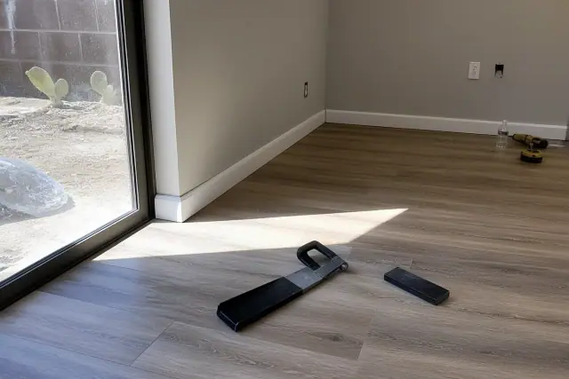 Newly installed laminate flooring and baseboards in a Tempe, AZ basement with a tapping block and pull bar nearby.