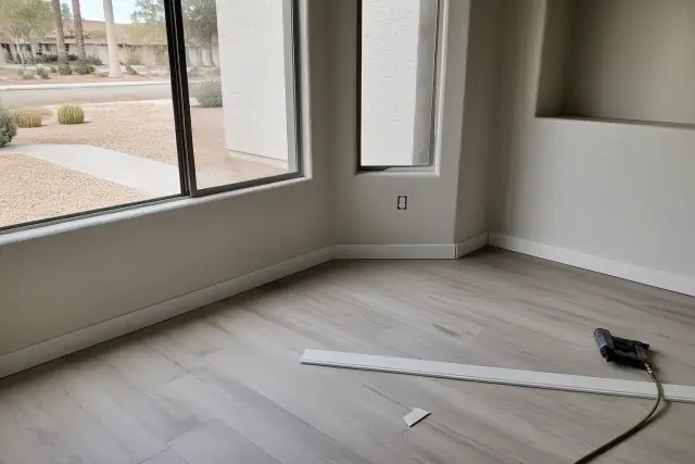 Laminate flooring and baseboards being installed in a room with a view of a desert xeriscaped yard in Phoenix, AZ.