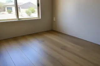 Laminate flooring planks meeting the wall edge with a view of a stucco home and xeriscaped yard in Phoenix, AZ.