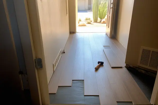 Luxury vinyl planks being installed in a hallway in Gilbert, AZ, with a view of a sun-drenched desert yard outside.