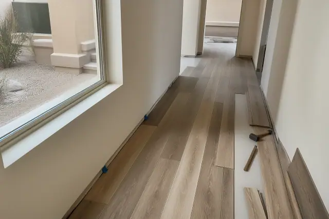 Worker installing luxury vinyl plank flooring in a narrow hallway of a home in Phoenix, AZ.