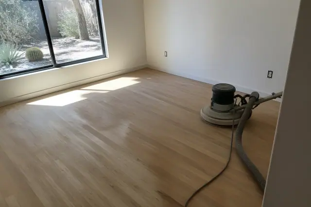 Buffing machine sanding hardwood floors in a Phoenix, AZ bedroom with desert landscape visible through the window.