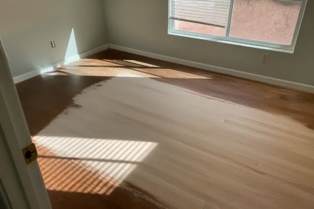 Hardwood floor planks in a bedroom during the sanding process in Phoenix, AZ, with sunlight casting shadows.