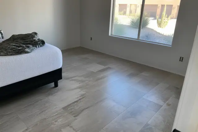Stone-look laminate flooring installed in a residential bedroom in Phoenix, AZ, with a window view of desert landscaping.