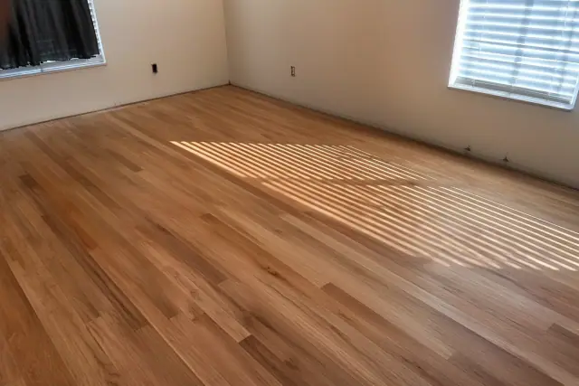 Hardwood floor planks showing natural grain and dust in a room with sunlight from blinds in Phoenix, AZ.