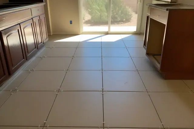 Spacers between new ceramic floor tiles in a kitchen in Avondale, AZ, with bright sunlight and nearby prickly pear cactus.
