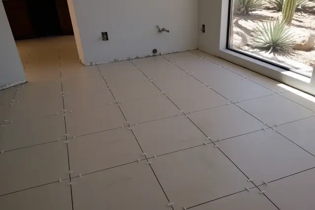 Spacers placed between ceramic floor tiles during a renovation project in Glendale, AZ with desert views through a window.