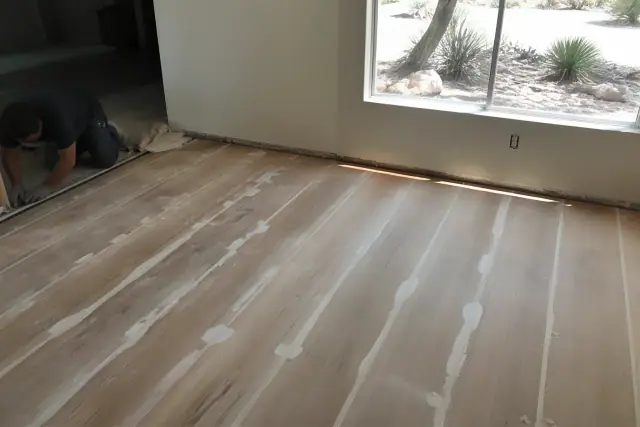 Contractor applying wood filler between floorboards during subfloor preparation in a Phoenix, AZ living room.
