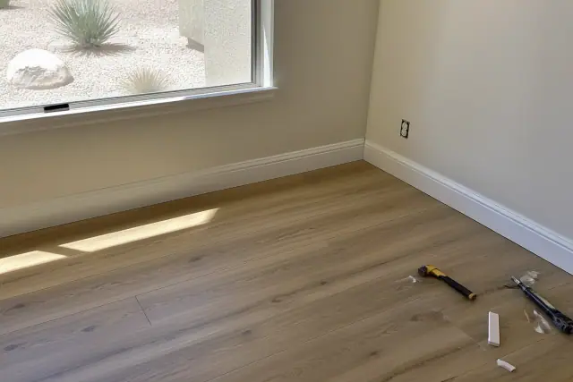Wood-look laminate flooring installation with baseboard trim in a sunlit room in Phoenix, AZ.
