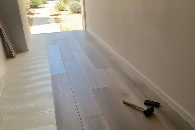 Worker installing wood-look vinyl plank flooring in a narrow Phoenix, AZ hallway with bright desert light.