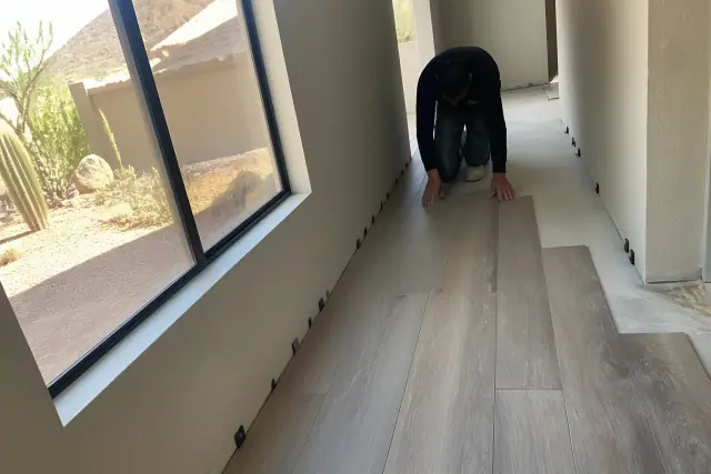 A contractor installing WPC luxury vinyl plank flooring in a narrow hallway in Phoenix, AZ.