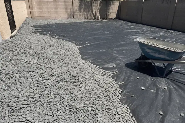 Decorative rock installation in progress on black weed barrier fabric in Phoenix, AZ.