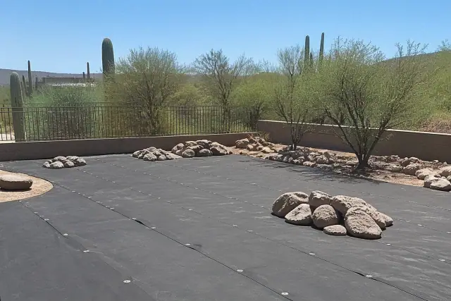 Weed barrier fabric installation for a desert landscaping project in Cave Creek, AZ with boulders and cacti.