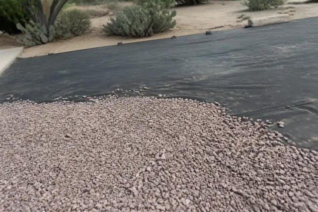 Fresh granite gravel being spread over weed barrier fabric at a landscaping job site in Phoenix, AZ.
