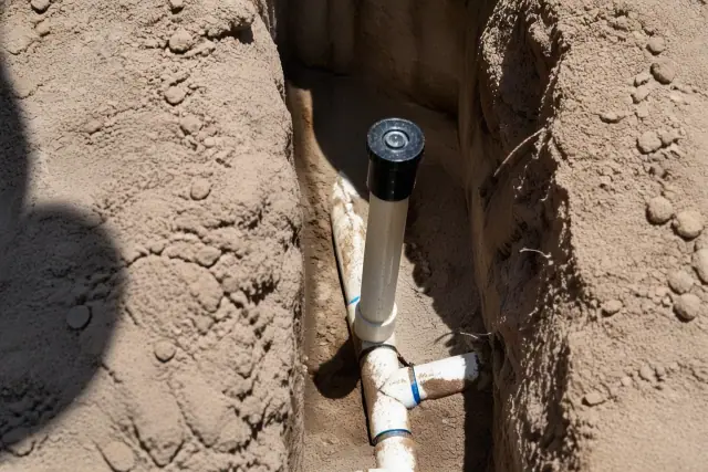 A technician repairing a sprinkler head and riser in an open trench in Phoenix, AZ.