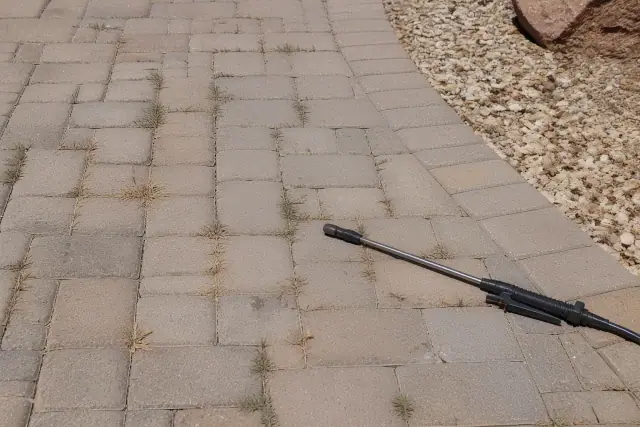 Handheld sprayer wand on pavers next to weeds in a Tempe, AZ landscape with crushed granite.