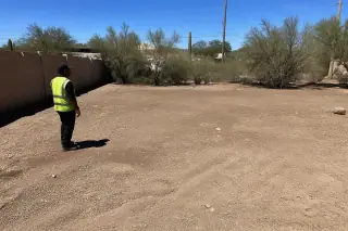 Worker inspecting a cleared landscape with desert shrubs and gravel in Phoenix, AZ.