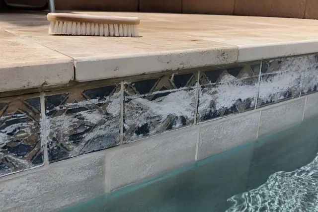 Calcium scale removal on pool tiles in Phoenix, AZ, showing scraped mineral residue and a cleaning brush on the coping.