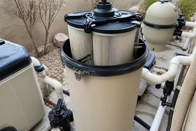 Opened pool filter housing with internal grid cartridges and plumbing at a residential jobsite in Phoenix, AZ.