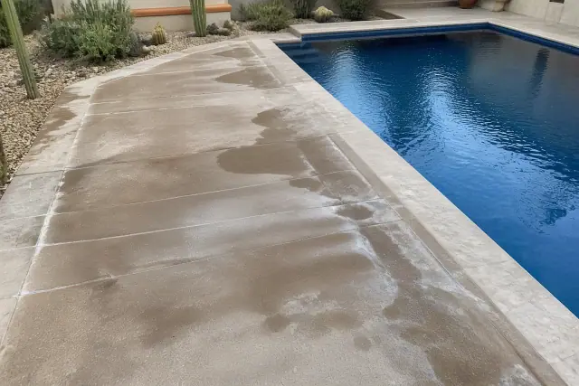 Pool deck surface showing residue lines and damp patches after cleaning in Phoenix, AZ, with desert landscaping nearby.