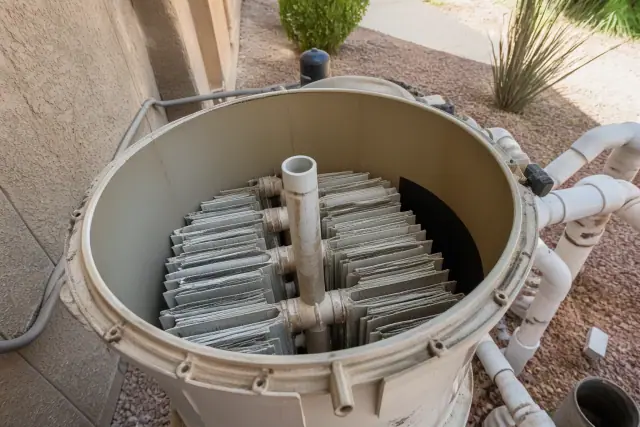 Opened pool filter housing with grid cartridges at a job site in Phoenix, AZ, with desert landscaping in the background.