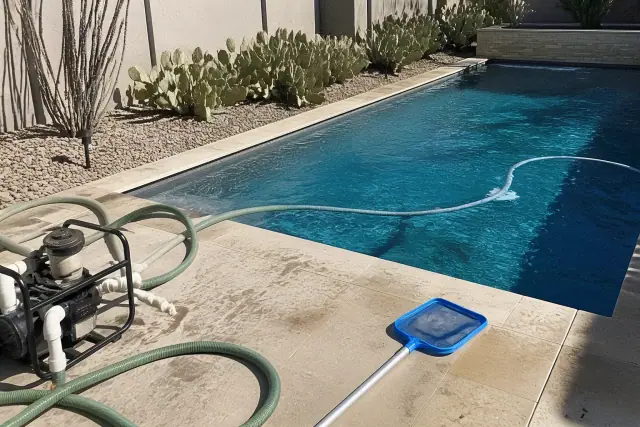 A pool technician cleaning a green pool with a long-handled net on a sunny deck in Scottsdale, AZ.