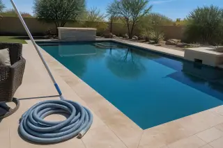 Coiled vacuum hose on the deck next to a clean rectangular pool in a Phoenix, AZ backyard.