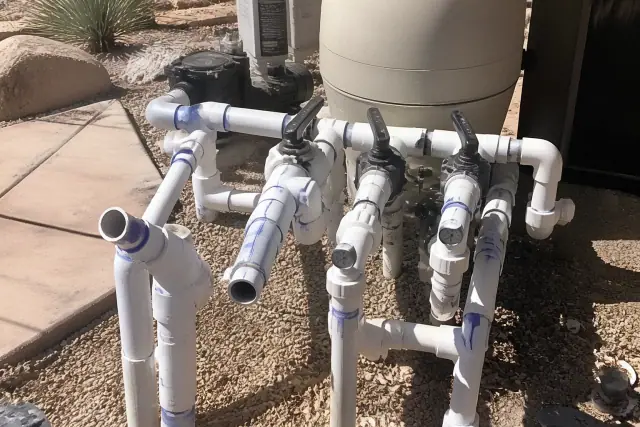 A pool plumbing manifold under repair with PVC pipes and gauges in Phoenix, AZ.