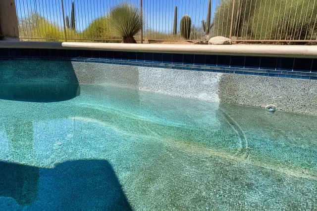 Acid-washed pebble and quartz pool surface in Phoenix, AZ, showing cleaning progress with cacti in the background.