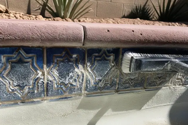 Contractor scrubbing calcium deposits from pool tiles in Phoenix, AZ.