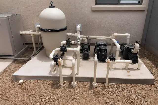 Pool equipment including filtration tanks, pumps, and plumbing lines on a concrete slab in a Phoenix, AZ backyard.