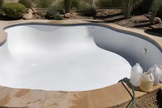 Acid-washed white plaster pool floor with a rinsing hose on the stone coping in a Phoenix, AZ backyard.
