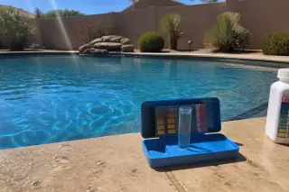 Digital water testing kit and chemical bottle on travertine pool coping in a Phoenix, AZ backyard.