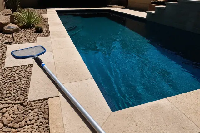 Pool cleaning in progress with a skimmer pole by a rectangular pool in Mesa, AZ.