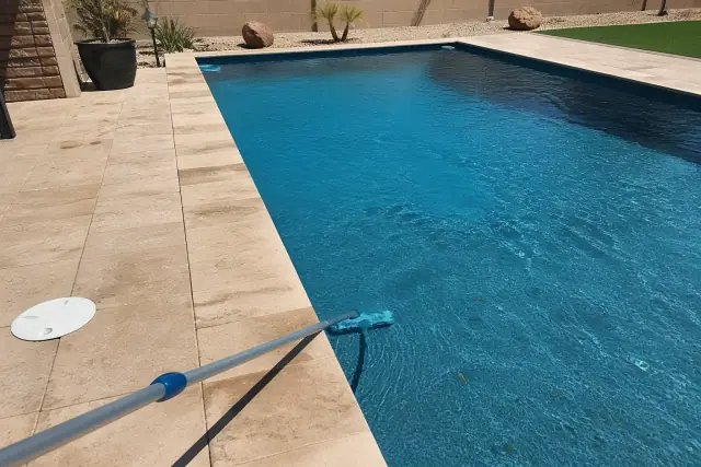 A technician cleaning a rectangular swimming pool with a vacuum pole at a residential home in Gilbert, AZ.